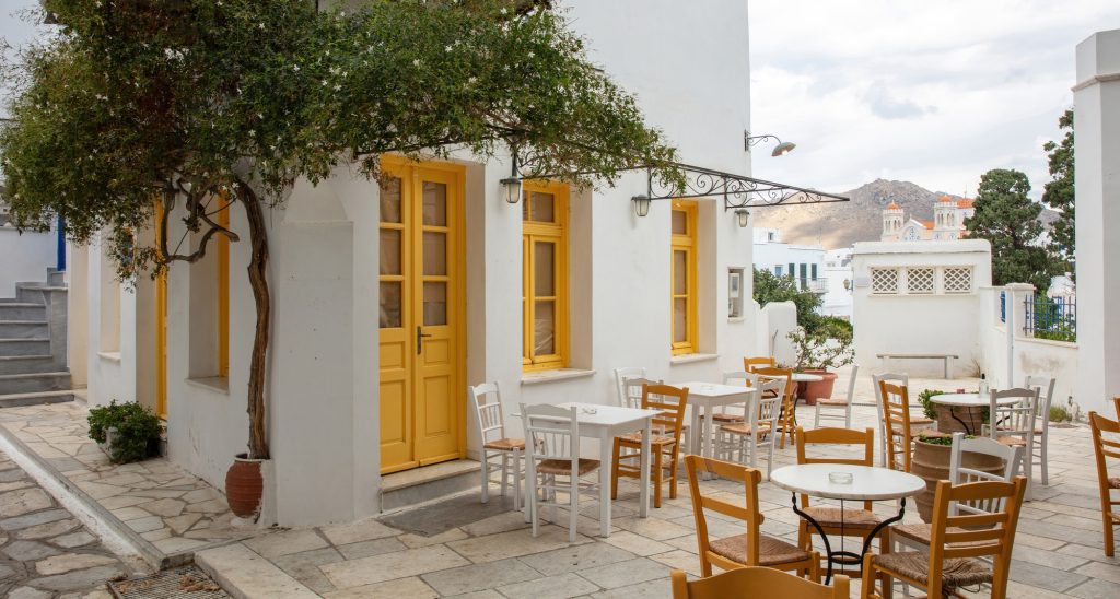 Greece. Tinos island Cyclades. Outdoors traditional cafe with yellow windows at Pyrgos village. Empty chair and table on paved yard — Photo