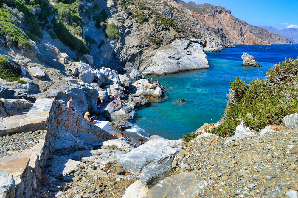 People sunbathing on the rocks in Agia Anna beach at Amorgos island of Greece - nastaszia / shutterstock