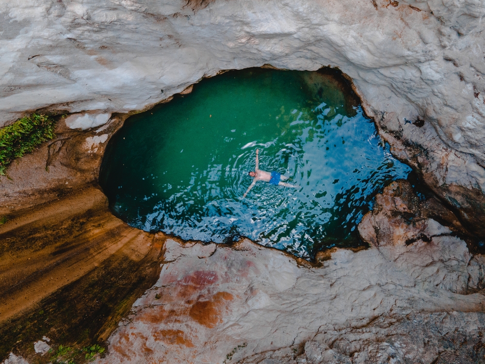 overhead view of dimosari waterfall lake with happy man floating on the back Lefkada island Greece -  Vera Petrunina / shutterstock